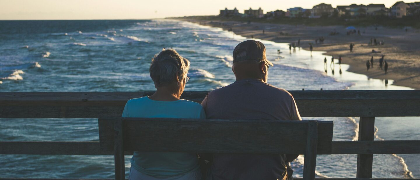 Retired couple sitting on a bench on a pier overlooking a beach