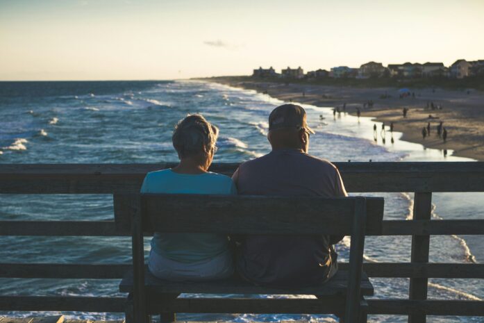 Retired couple sitting on a bench on a pier overlooking a beach
