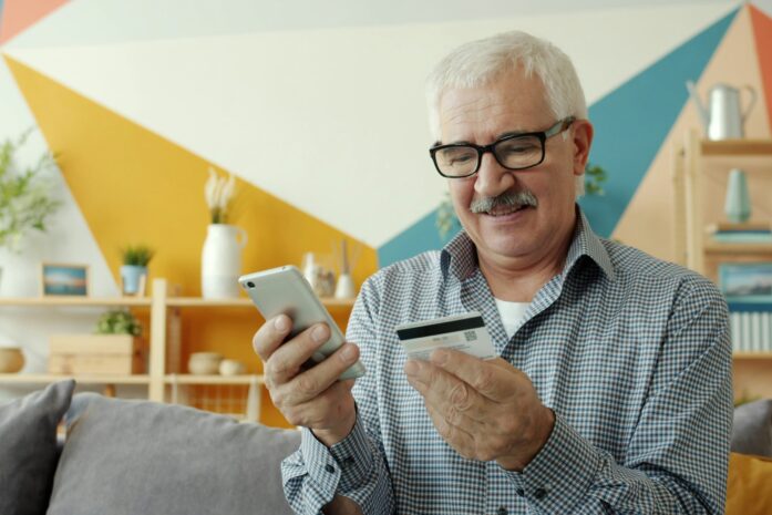 Smiling retired man looking at his mobile phone and credit card