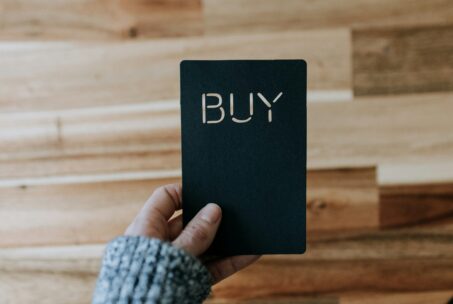 A hand holding a piece of paper with the word BUY cut into the paper